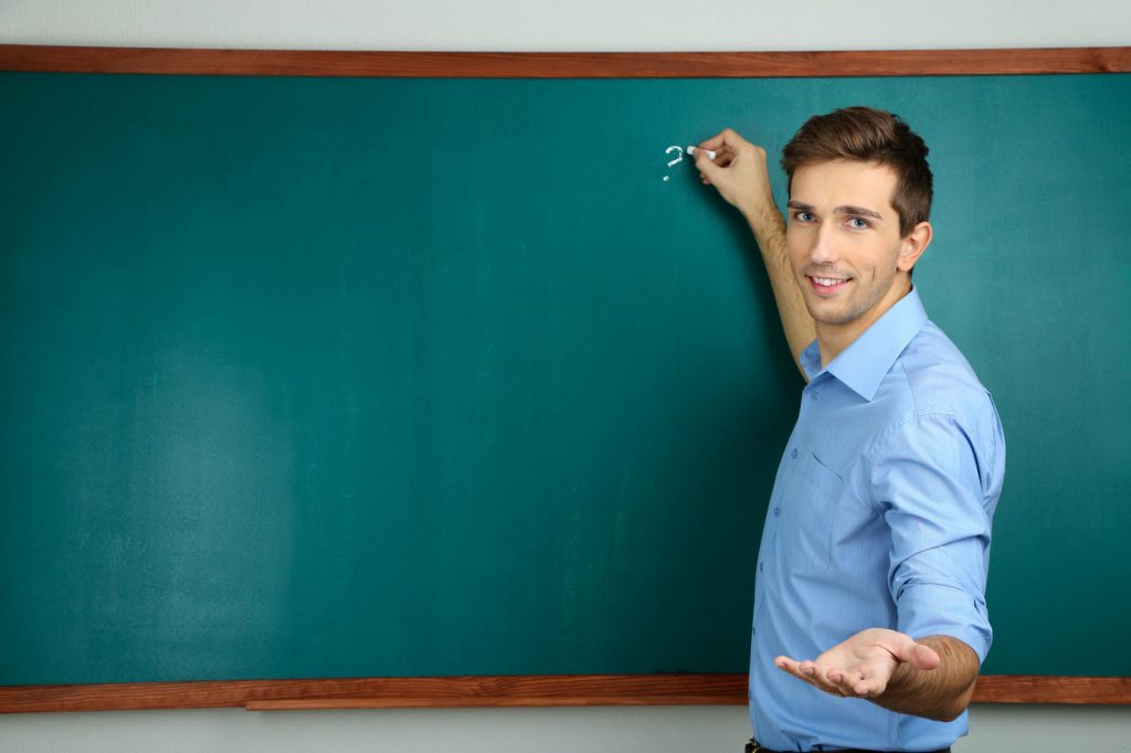 Young teacher near chalkboard in school classroom