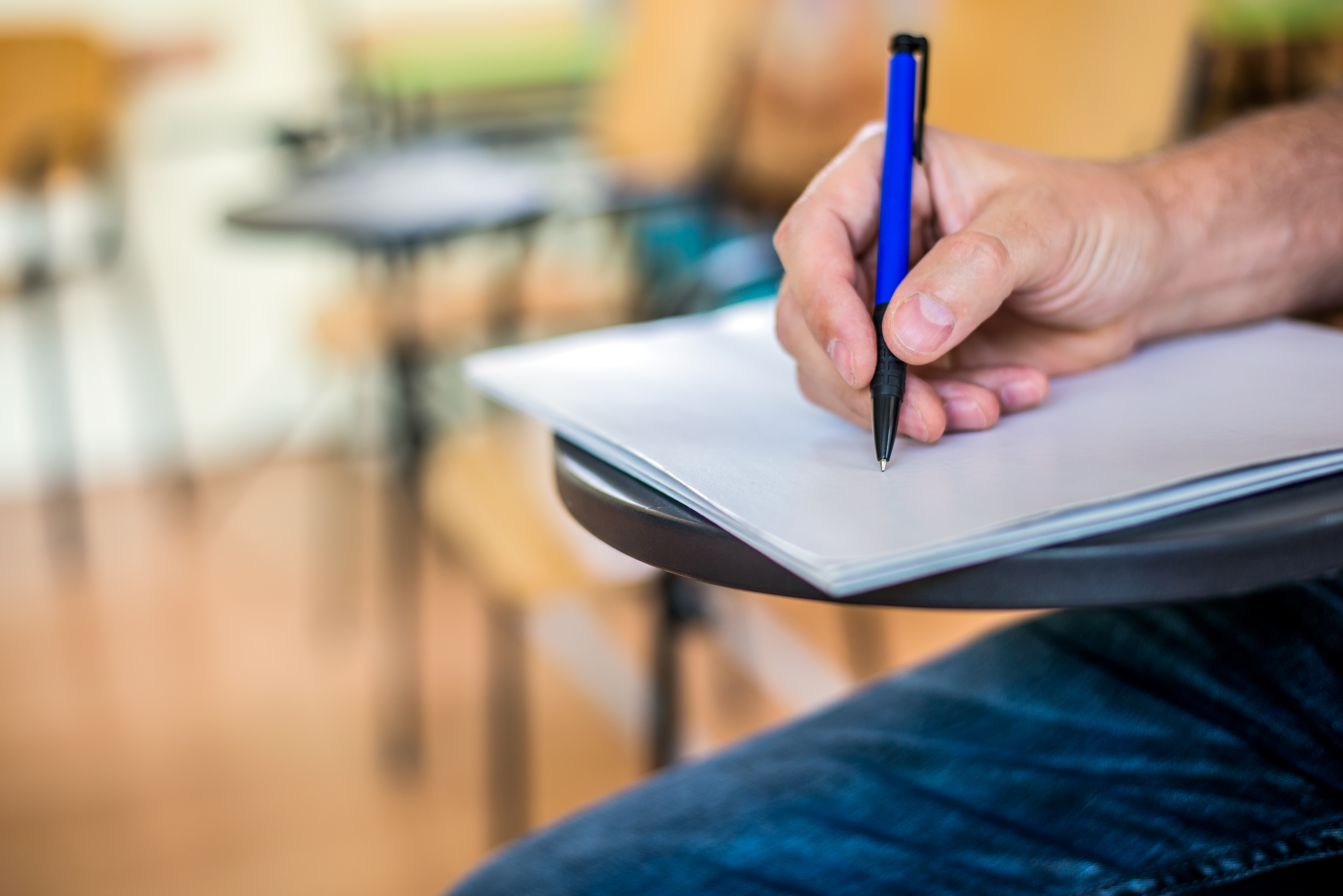 A man is writing/signing on a paper. Focused on a hand with pen. undergraduate student holding pencil and sitting on row chair doing final exam attending in examination room or classroom.university student.