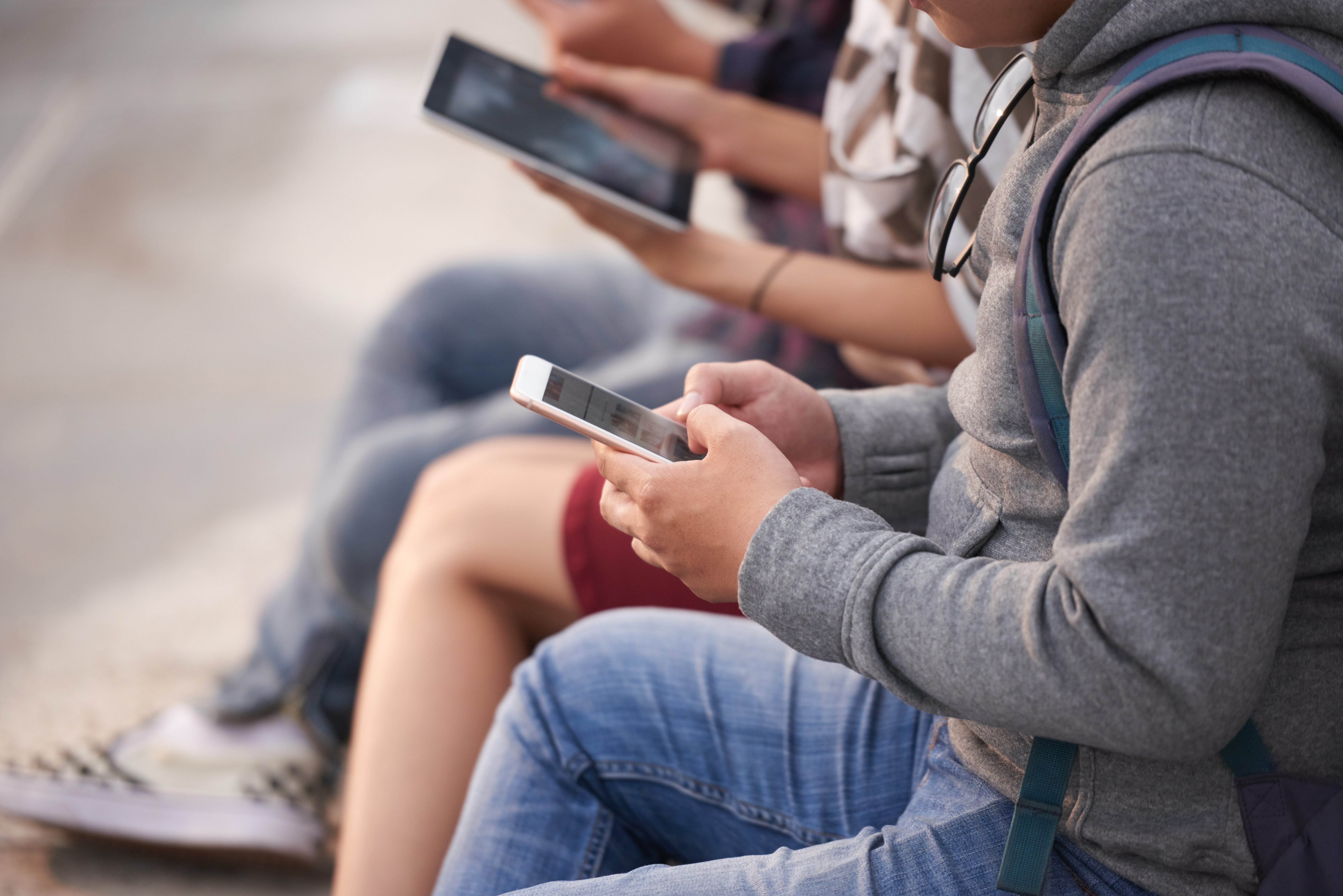 Unrecognizable group of friends in casualwear gathered together outdoors and using their devices, close-up shot